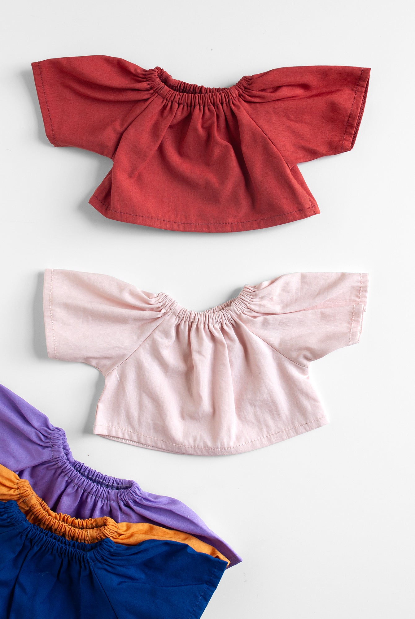 Set of four colorful tops with ruffled shoulders on a white background