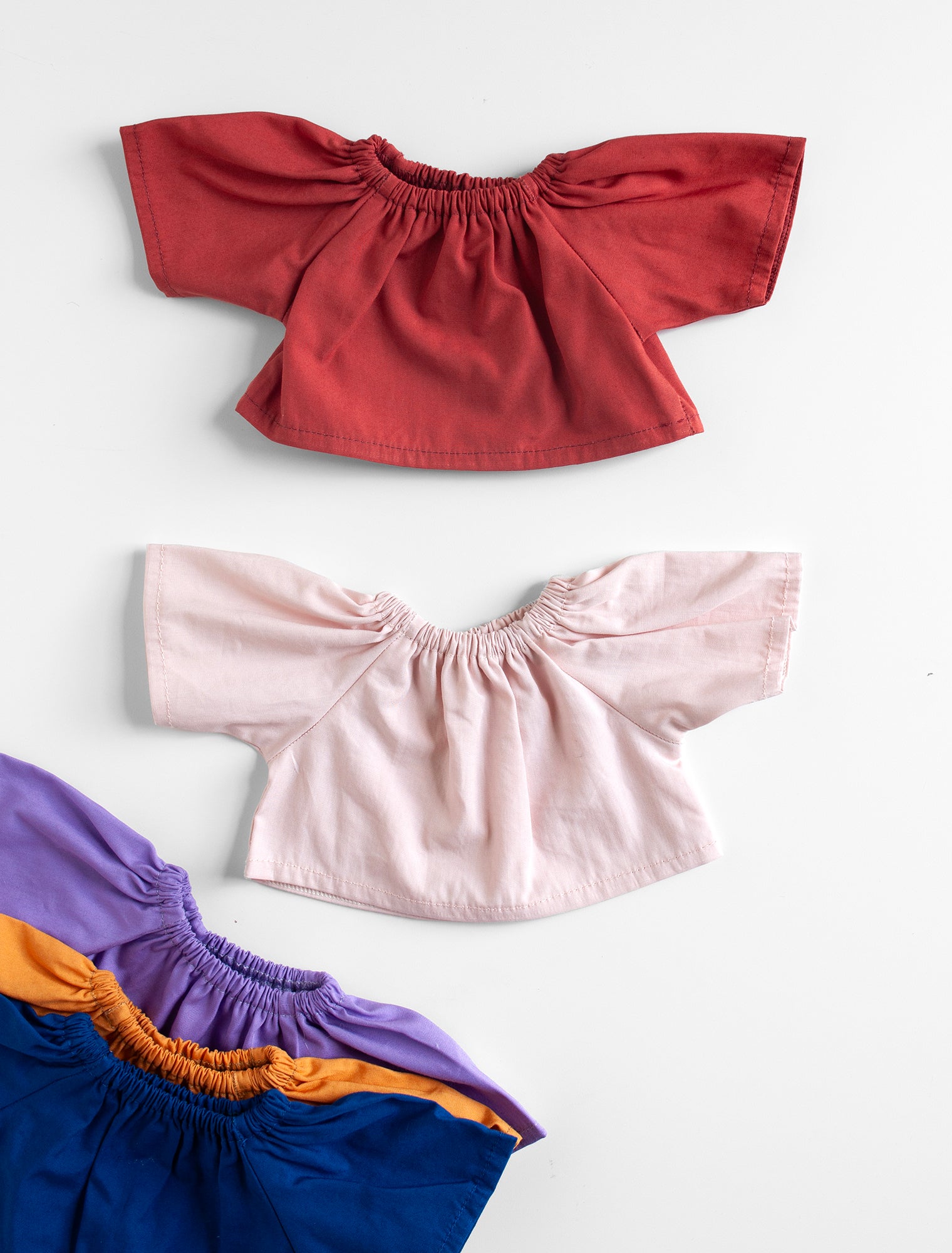 Set of four colorful tops with ruffled shoulders on a white background