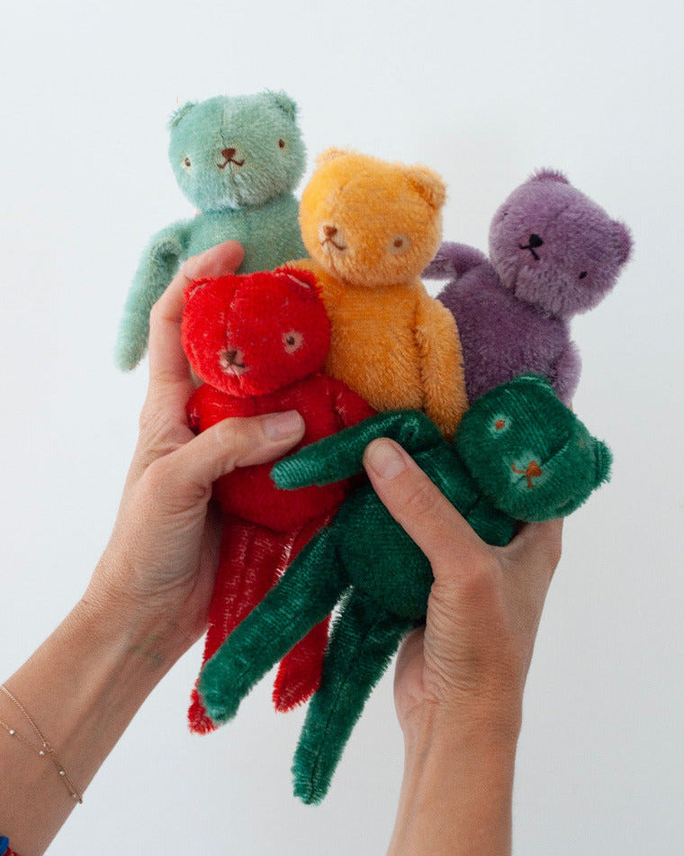 Hand holding four colorful PDC Floppy Bear toys against a white background